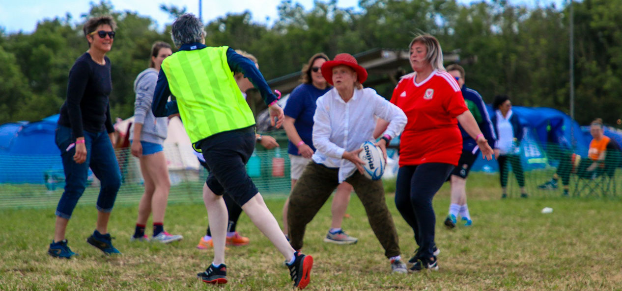 A group of women play football outdoors next to some camping tents.