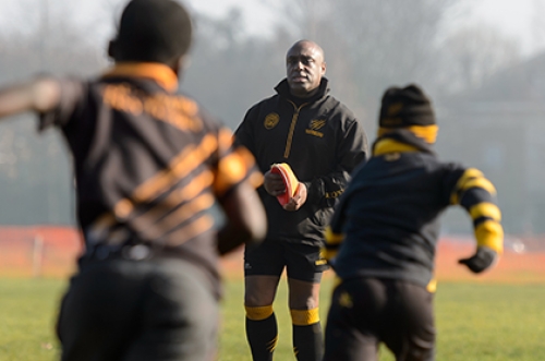 A junior rugby coach watches on as two players run towards him