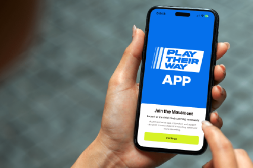 A hand holding a phone on which the Play Their Way app is displayed